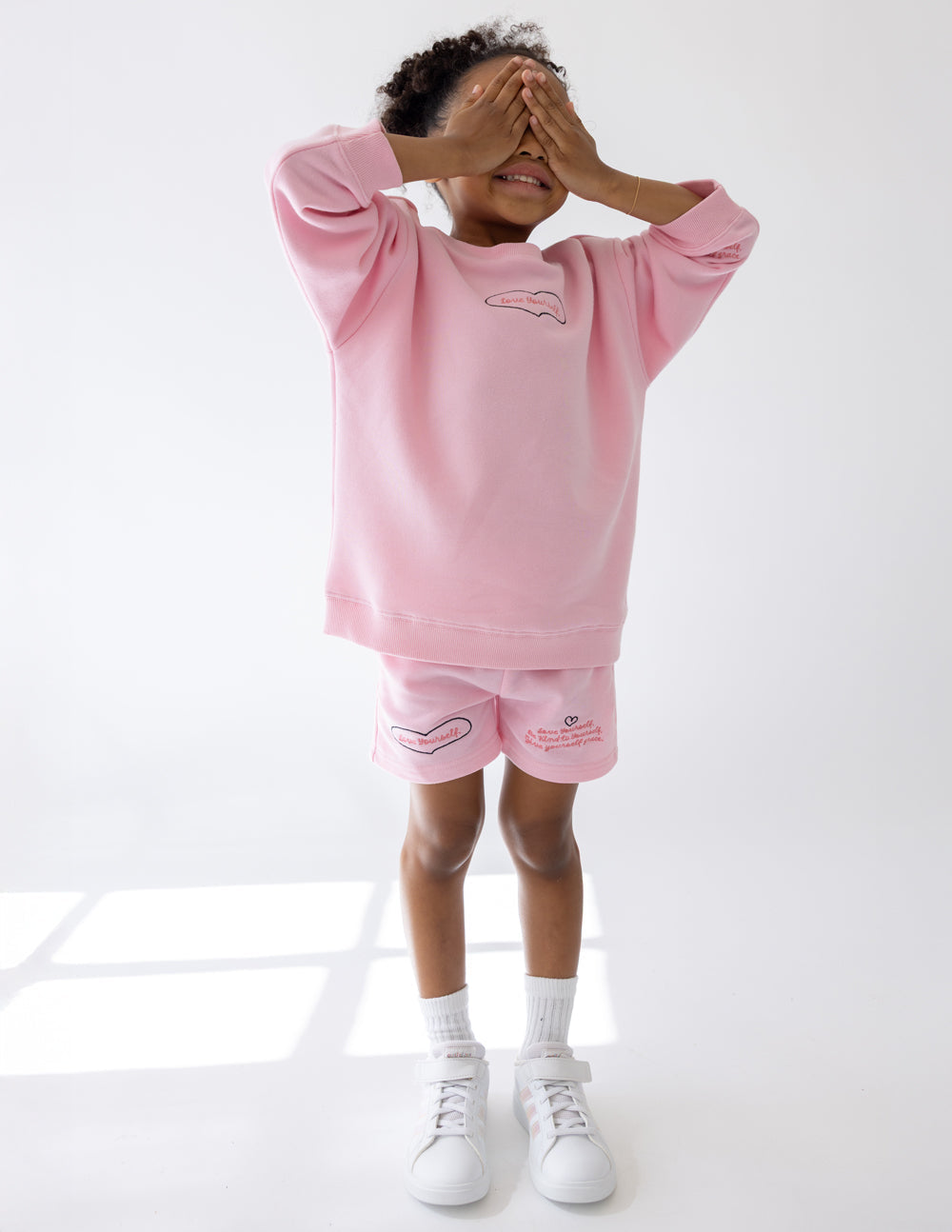 Kids pink crewneck sweatshirt with small heart graphic; long sleeves and ribbed cuffs