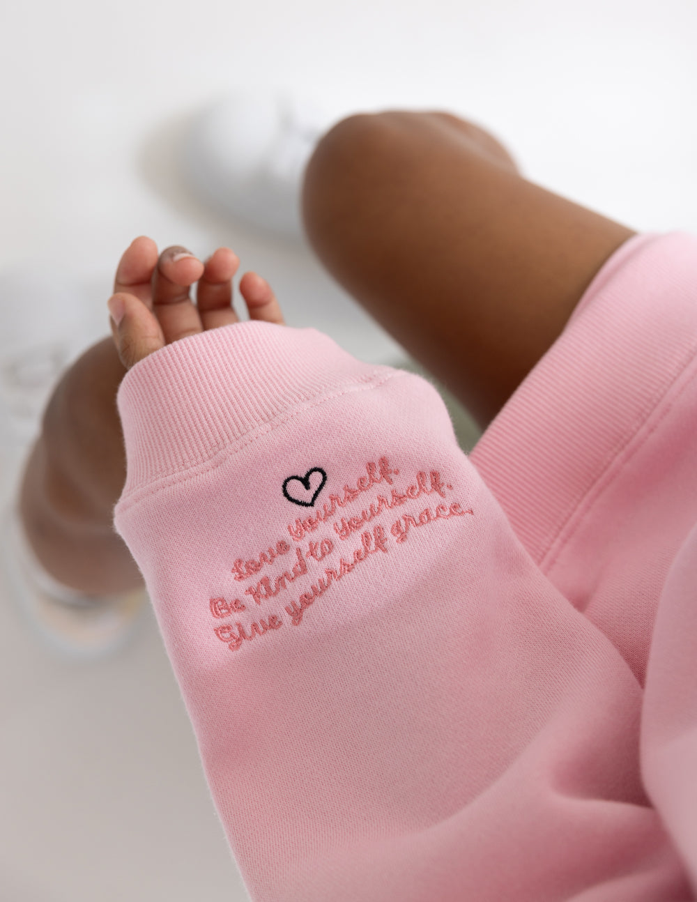 Pink sweatshirt cuff with embroidered “Love yourself” text and heart outline; ribbed edge