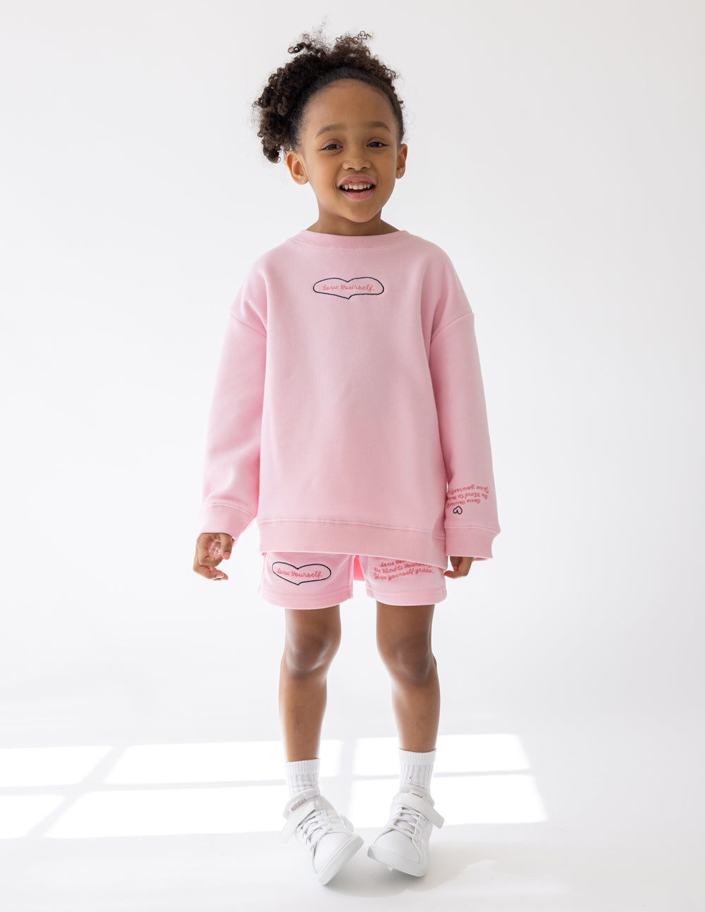 Kids pink crewneck sweatshirt with heart outline graphic; front view and ribbed cuffs