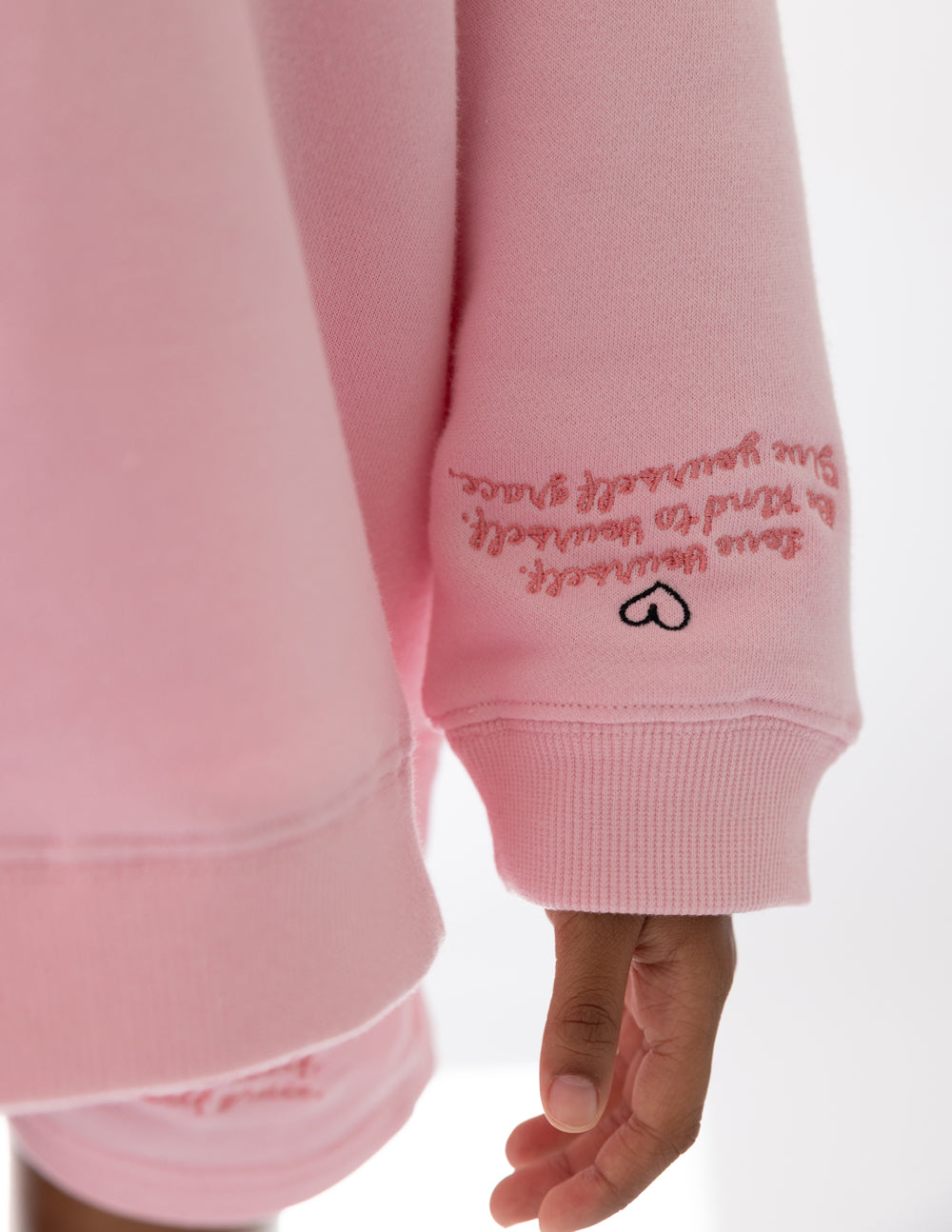 Pink sweatshirt sleeve cuff with embroidered text and peace-heart icon; ribbed hem