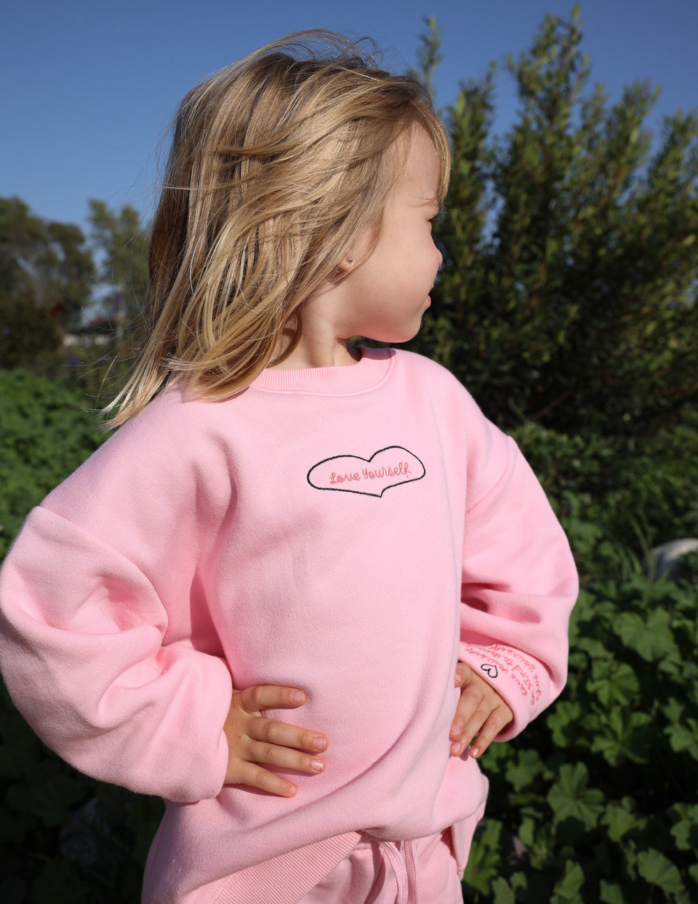 Kids pink crewneck sweatshirt back with small heart patch graphic; ribbed cuffs