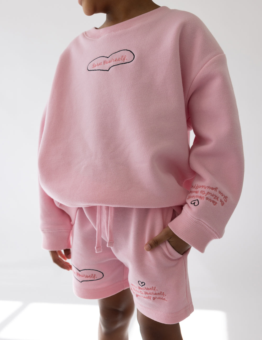 Kids pink shorts with drawstring waist, heart logo, and pocket detail on front