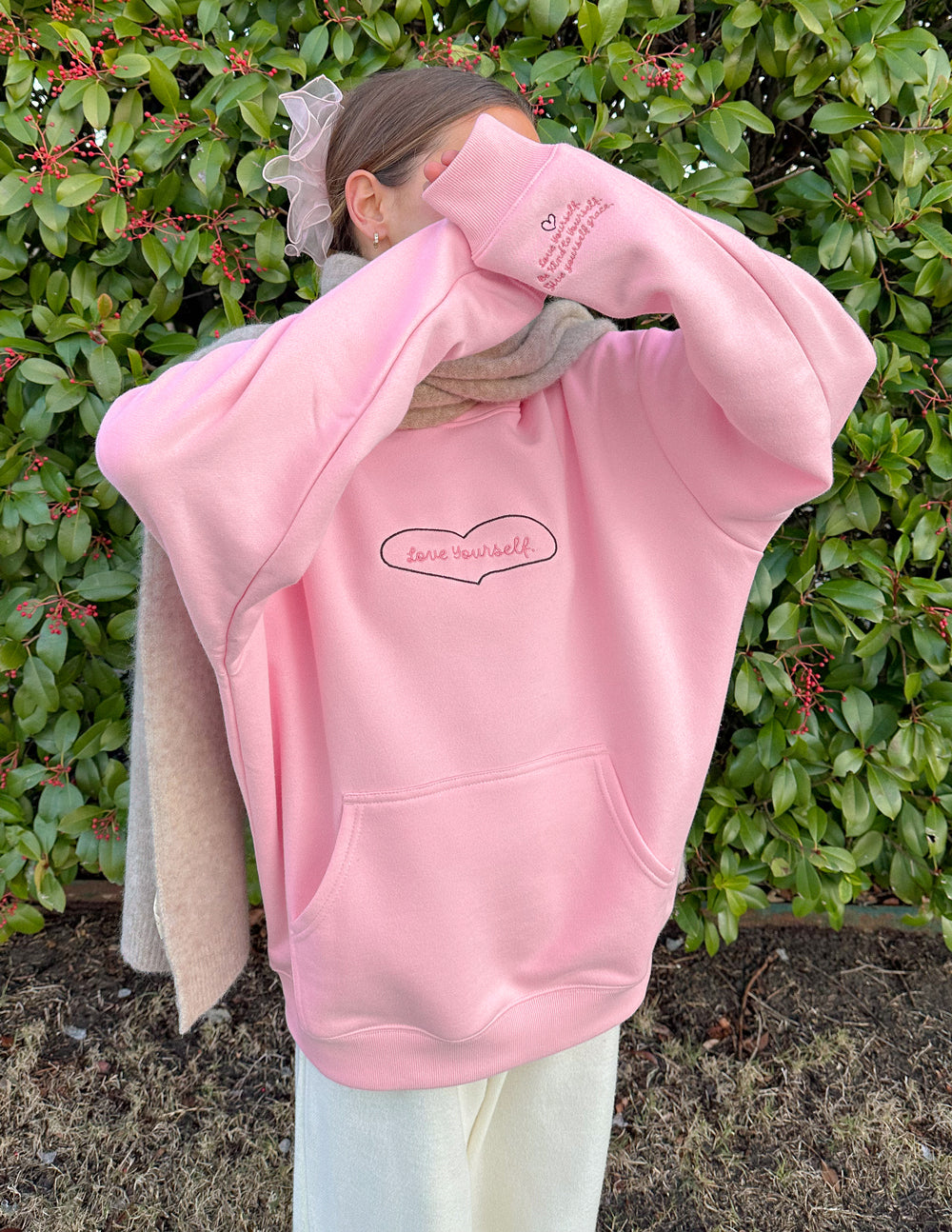 Pink unisex hoodie with hood and kangaroo pocket, with heart-shaped “Love Yourself” logo.