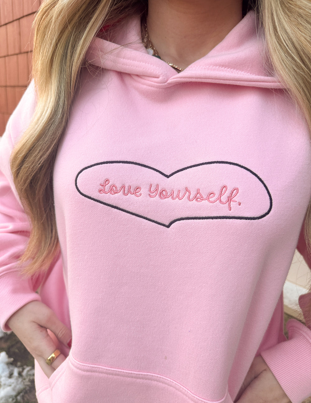 Pink hoodie front with heart-shaped “Love Yourself” logo across the chest.