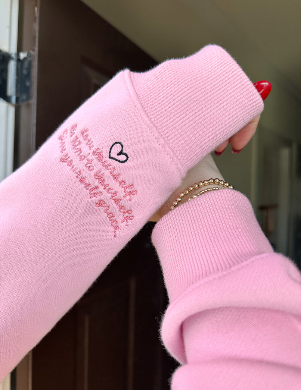 Pink hoodie sleeve with ribbed cuff and red “Love Yourself” text on the forearm.