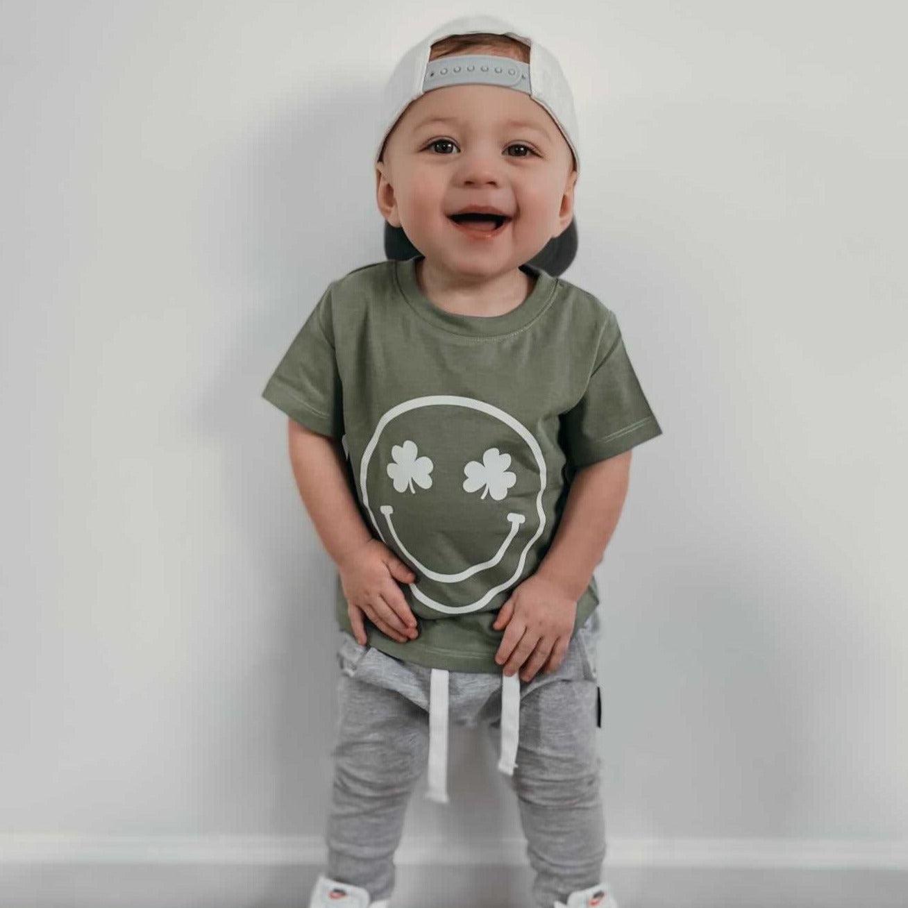 Green baby T-shirt with white smiley clover face graphic, short sleeves