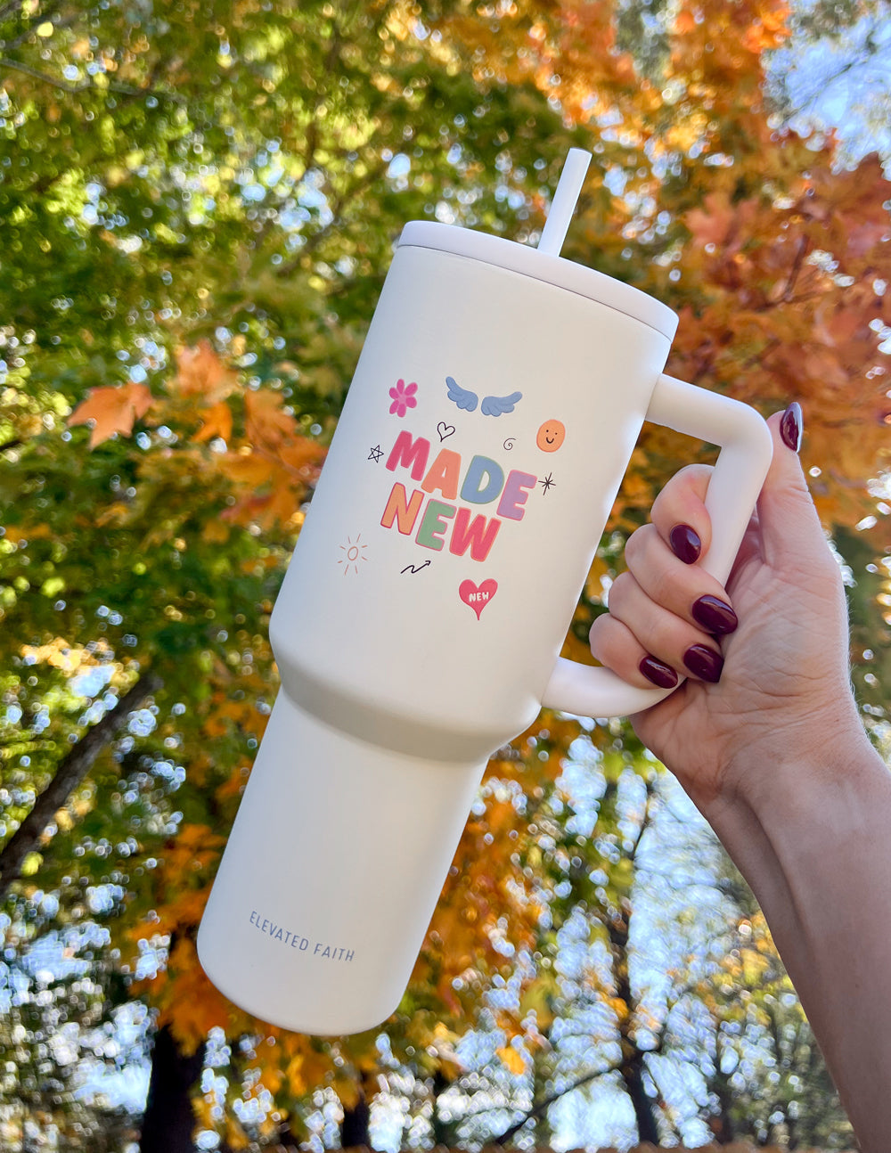 White 40 oz tumbler with handle and straw lid, “Made New” graphic, held in hand