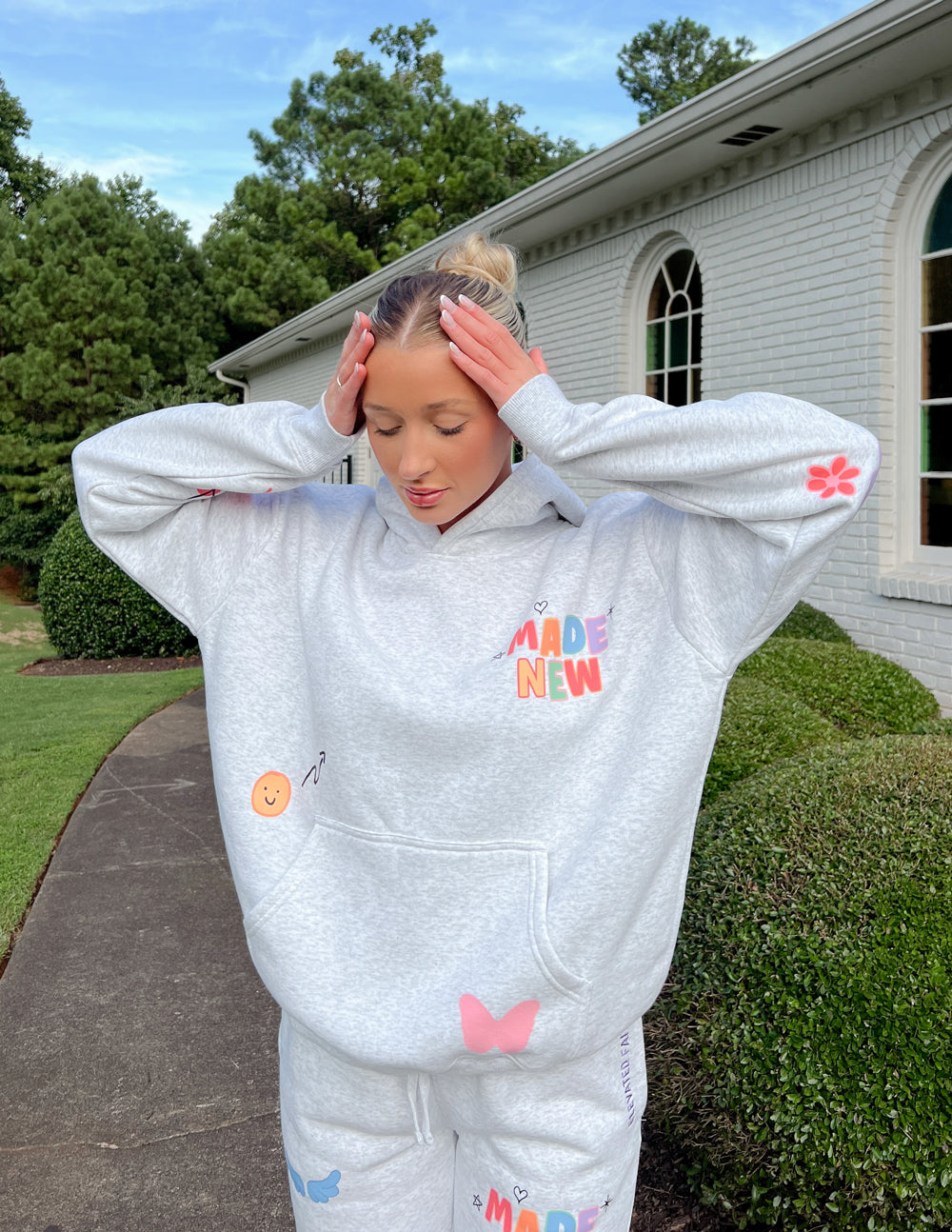Light gray unisex hoodie with red "Made New" chest graphic and colorful sleeve patches