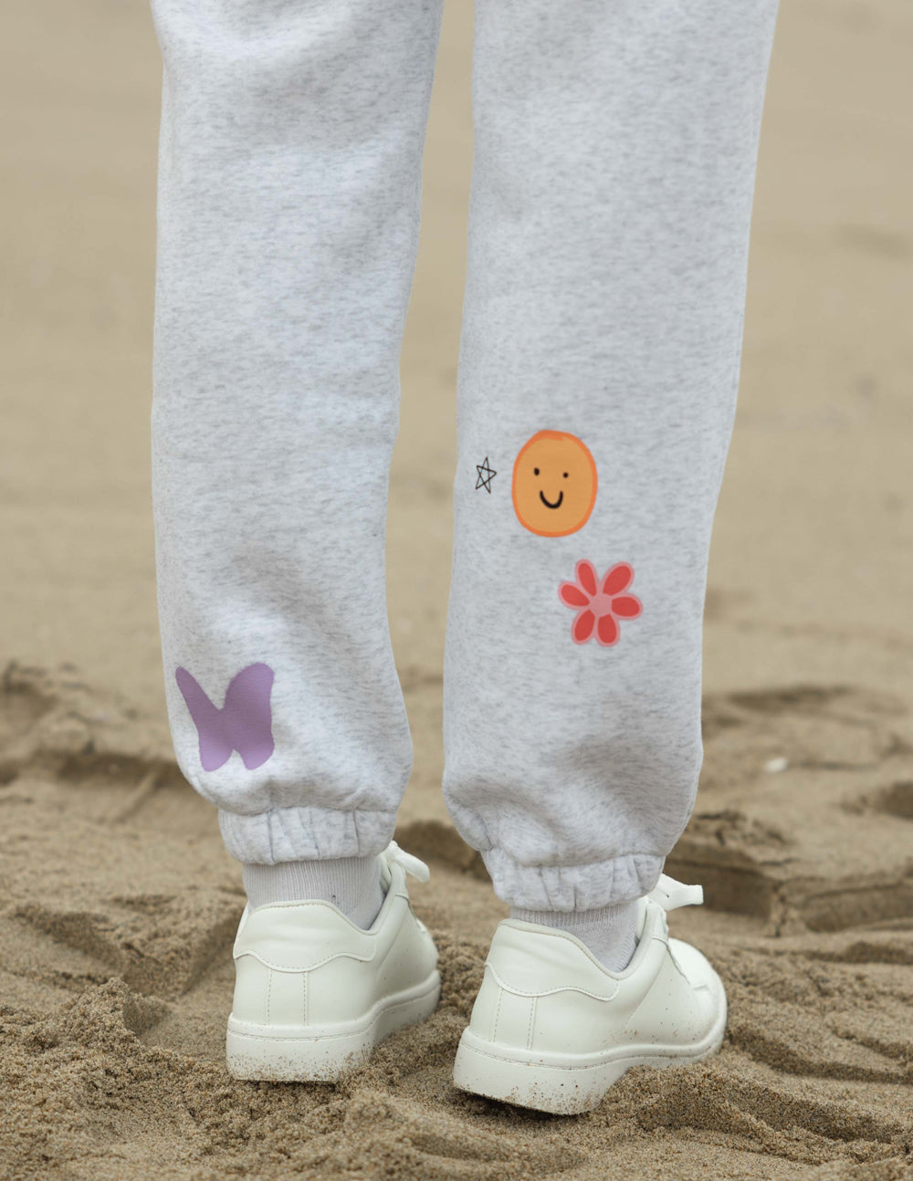 Heather gray sweatpants with butterfly, smiley, and flower prints on the lower legs