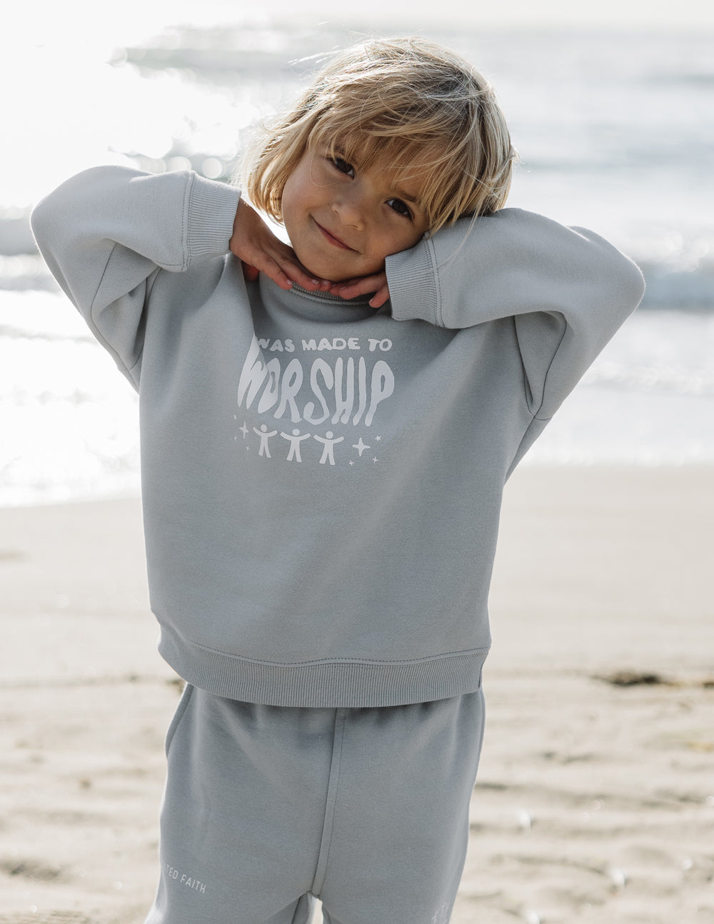 Kids crewneck sweatshirt, light blue with front “worship” graphic, hands behind head