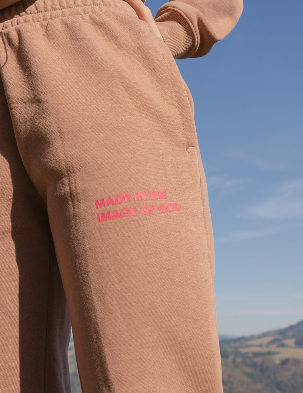 Brown unisex sweatpants close-up with red text logo on the leg