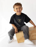 Black kids graphic tee worn by child, gold 'MADE IN THE IMAGE OF GOD' print