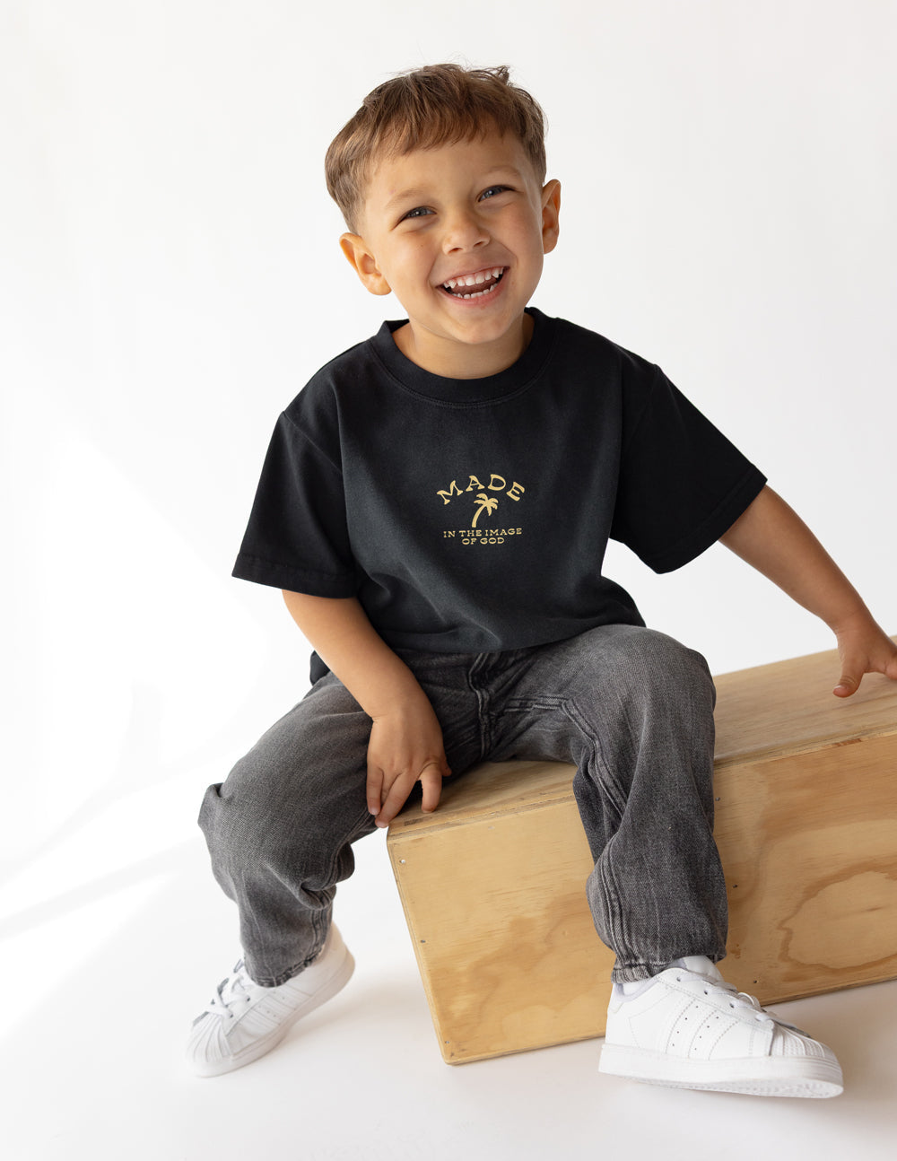 Black kids graphic tee worn by child, gold 'MADE IN THE IMAGE OF GOD' print