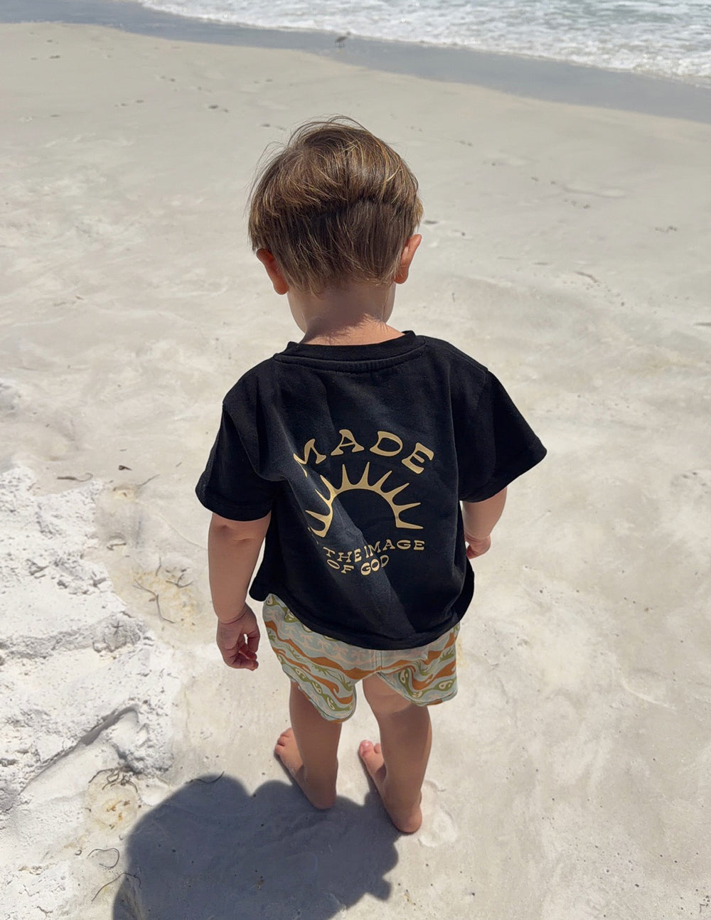 Kids black graphic tee showing the gold sunburst back design