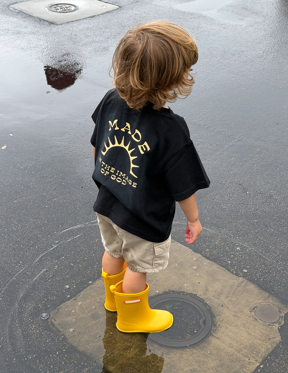 Kids black graphic tee back view with gold sunburst logo