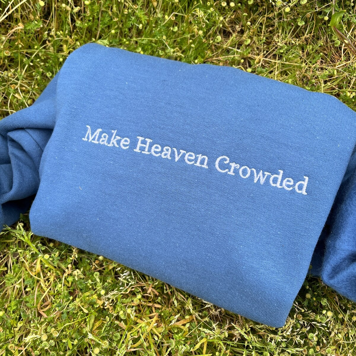 Blue sweatshirt back embroidered with text: Make Heaven Crowded
