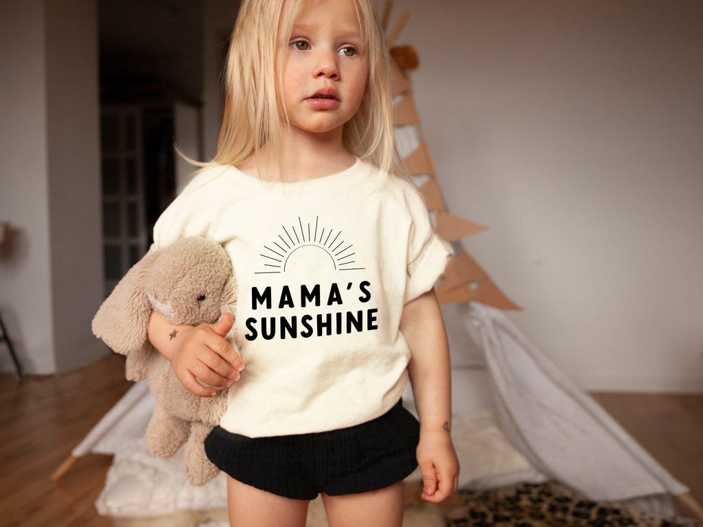 Cream baby T-shirt with “Mama’s Sunshine” sun graphic in dark print