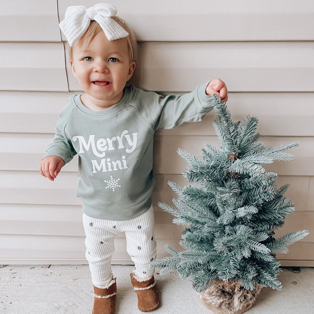 Sage green baby pullover sweatshirt with “Merry Mini” text and snowflake graphic