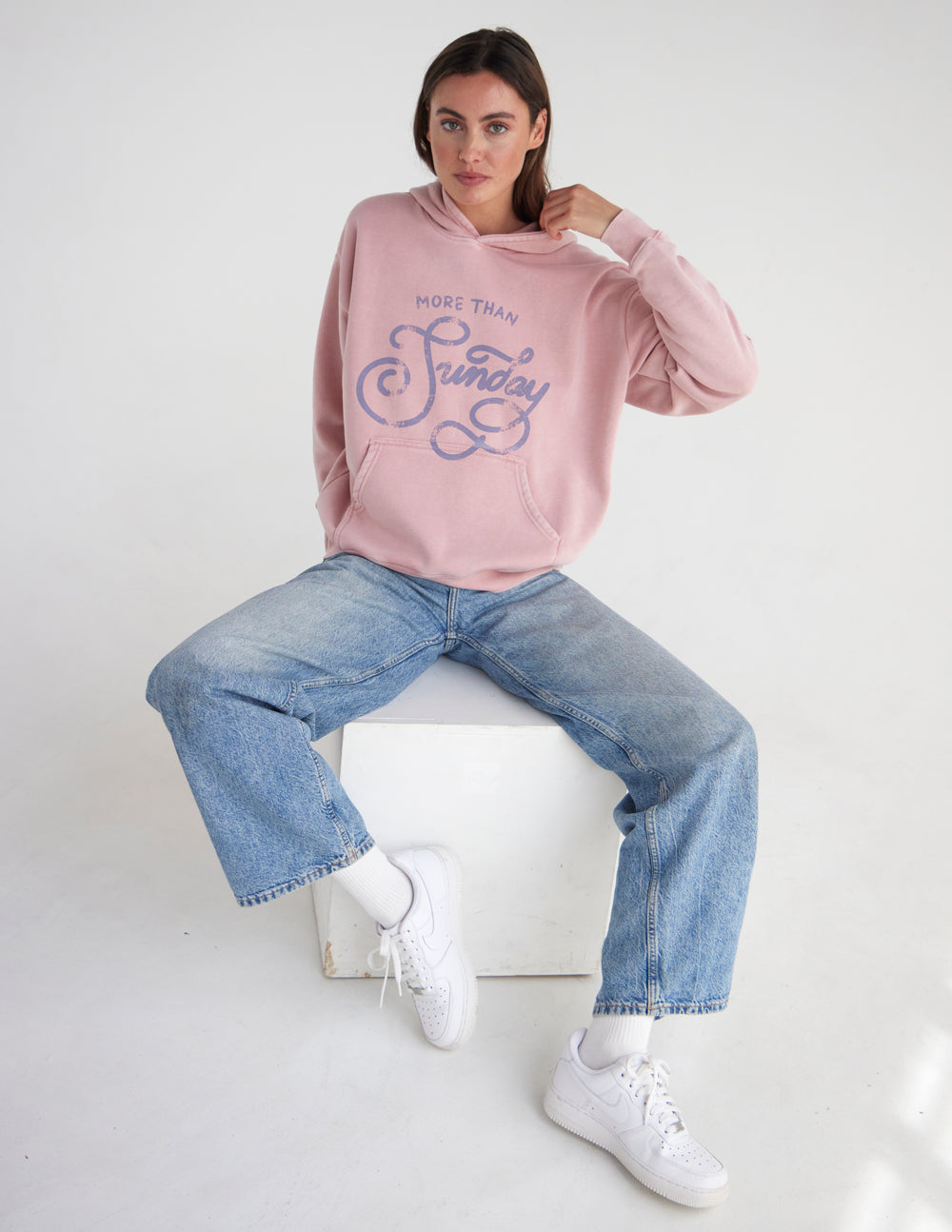 Unisex pink hoodie with hood and front logo graphic, relaxed seated pose