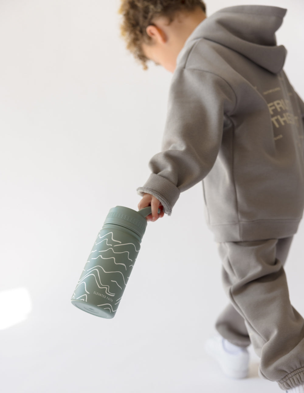 Kids water bottle held, sage green with white wave lines and flip spout