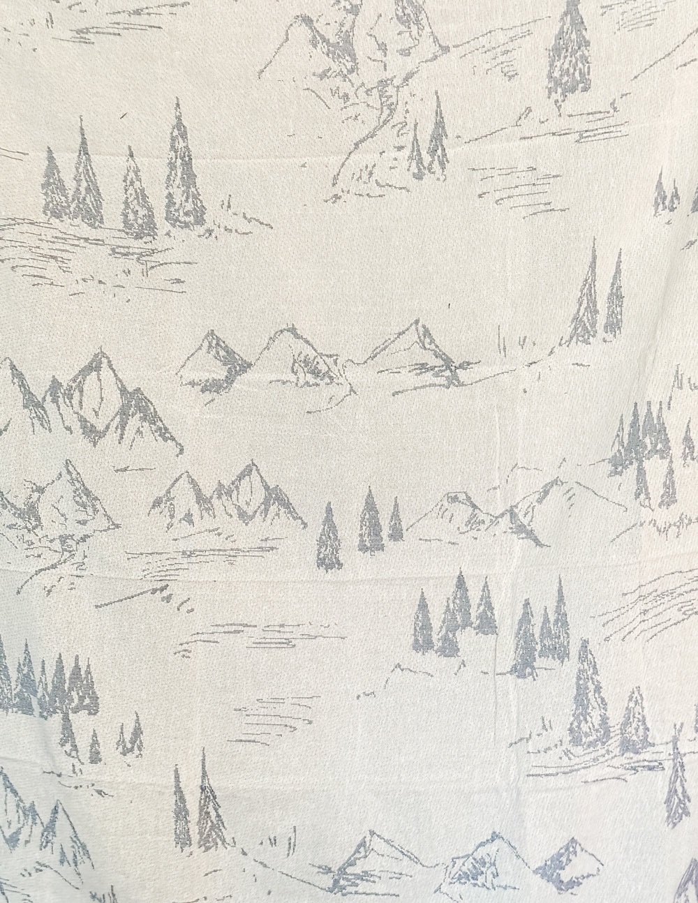 Cream throw blanket with blue mountain and pine pattern, close-up