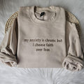 Beige crewneck sweatshirt laid flat with embroidered text: my anxiety is chronic but I choose faith