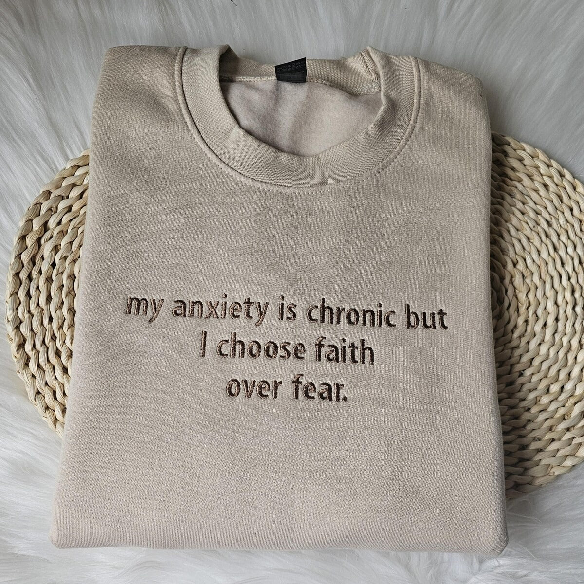 Beige crewneck sweatshirt with embroidered chest text: my anxiety is chronic but I choose faith