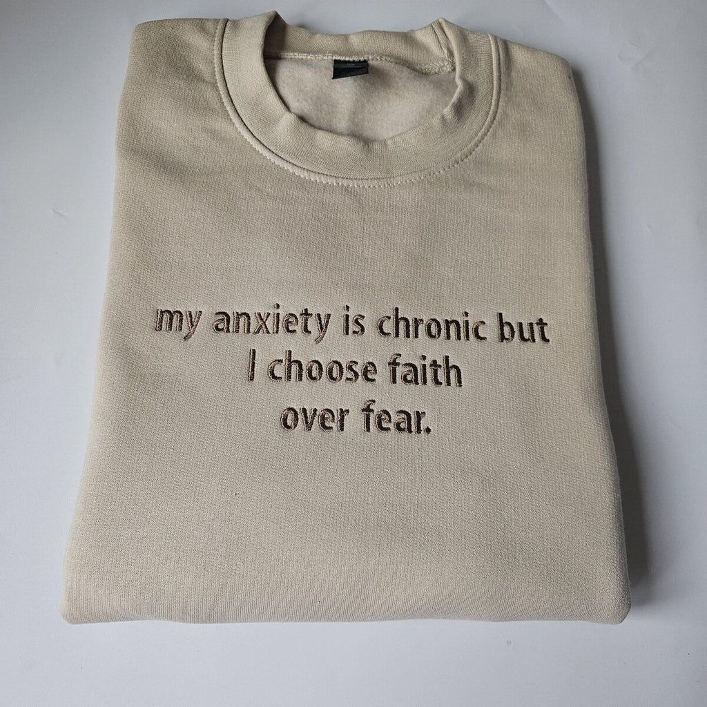 Beige crewneck sweatshirt with embroidered message: my anxiety is chronic but I choose faith