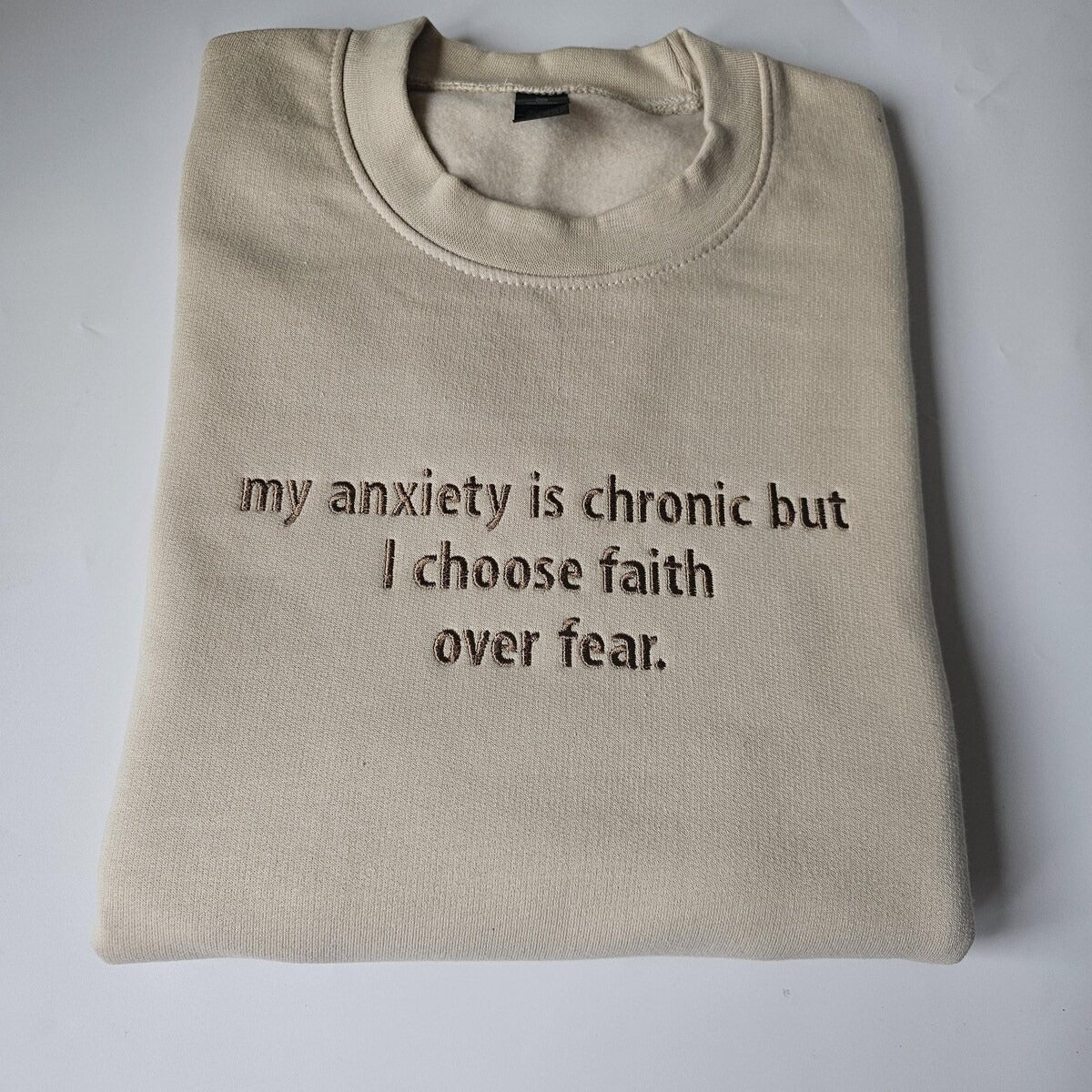 Beige crewneck sweatshirt with embroidered message: my anxiety is chronic but I choose faith