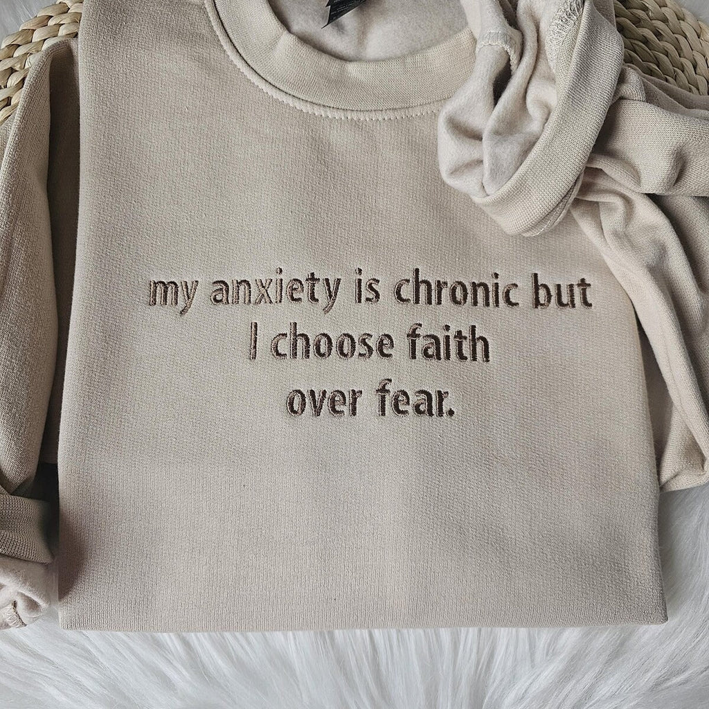 Beige crewneck sweatshirt close-up with embroidered text: I choose faith over fear