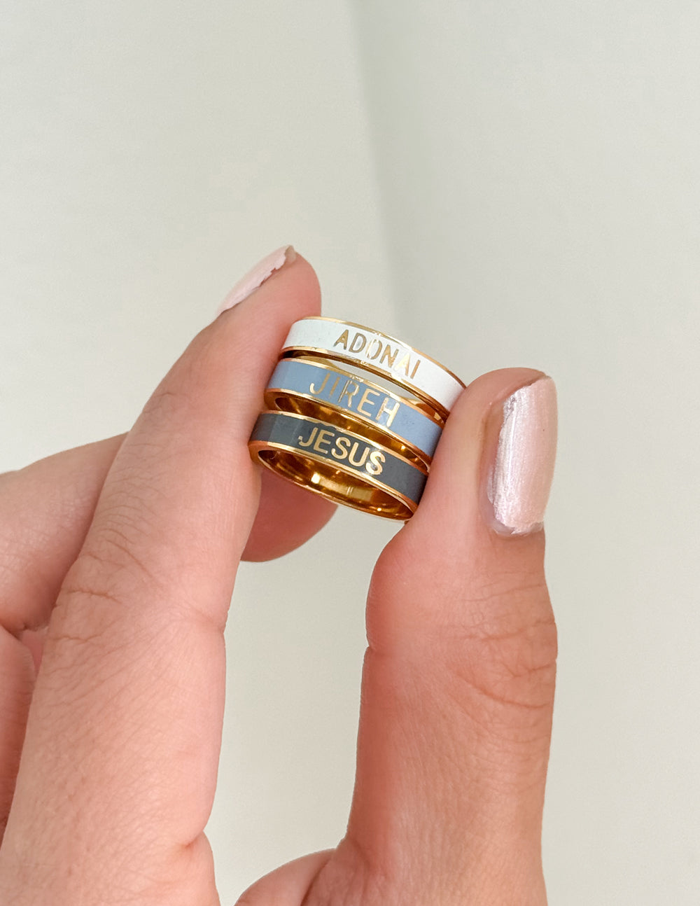Enamel stackable rings on fingers: ADONAI, JESUS, and JIREH in blue and black.