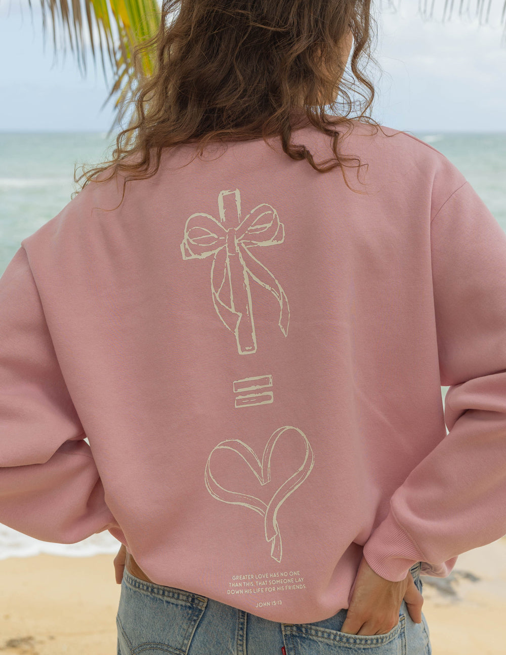 Pink sweatshirt with large back bow-and-heart graphic and small logo text near hem