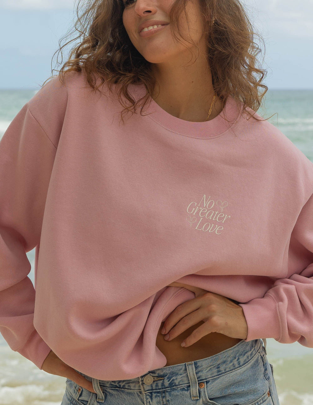 Pink crewneck sweatshirt with small chest logo graphic and ribbed collar, sleeves, and cuffs
