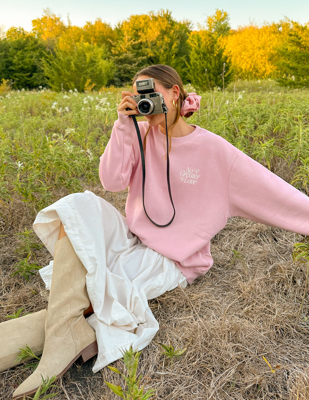 Pink unisex crewneck sweatshirt worn with white shirt peeking out, small chest logo print