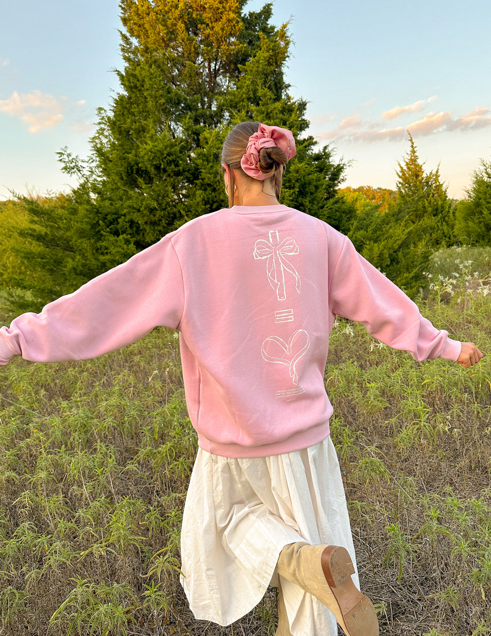 Pink sweatshirt back with bow-and-heart graphic and outlined text near lower back