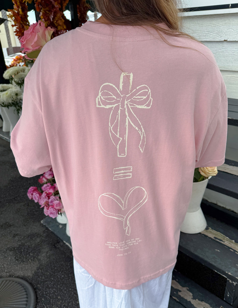 Unisex pink T-shirt with large back bow and heart line-art graphic.