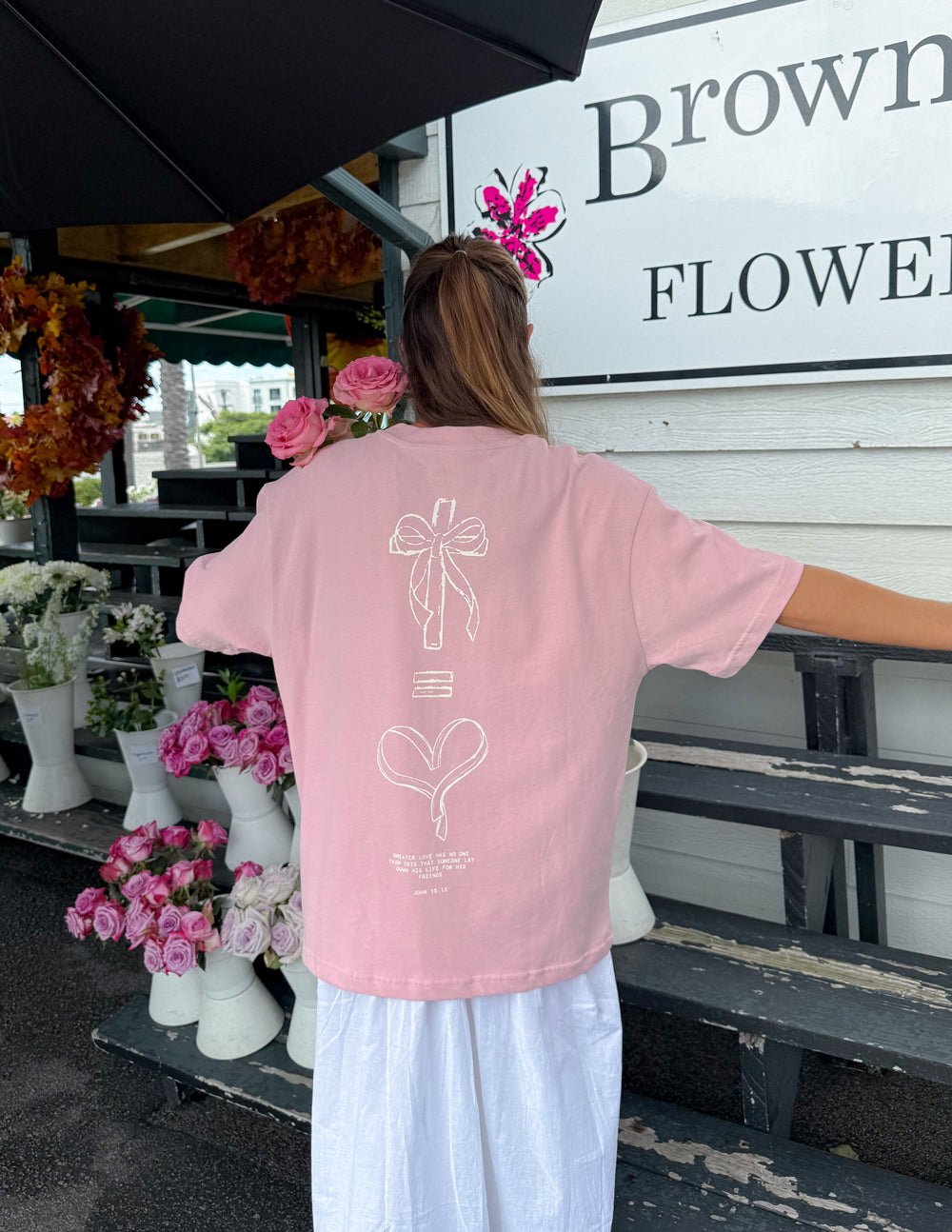 Unisex pink T-shirt back view with bow and heart line-art graphic.