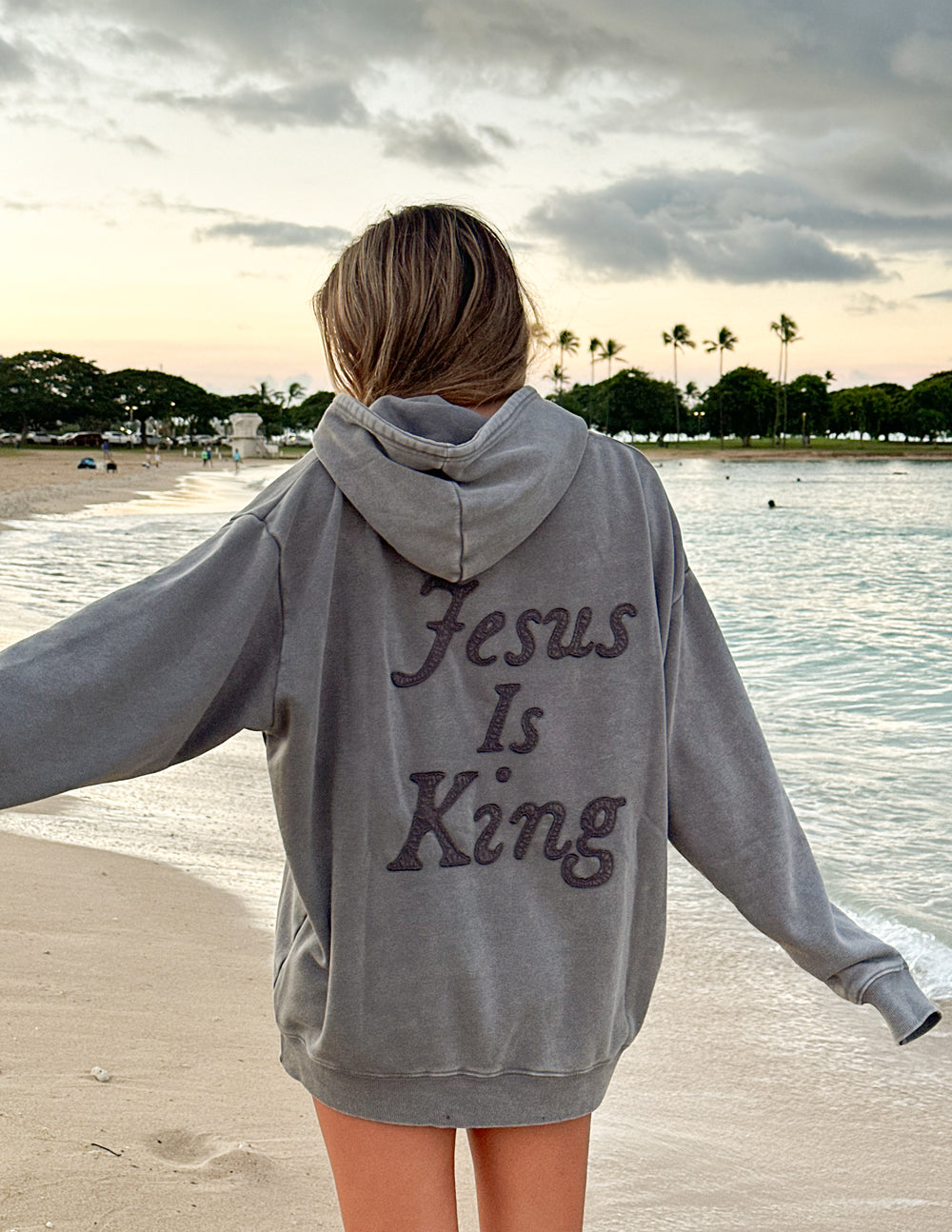 Gray unisex hoodie with hood up and large back script “Jesus Is King” print