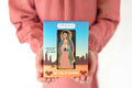 Guadalupe devotional card with illustrated Our Lady figure on blue cover and skyline