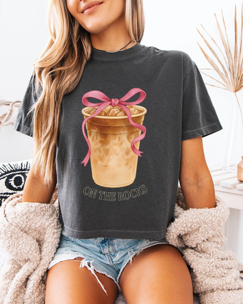 Women’s cropped T-shirt, charcoal black with pink bow latte graphic and 'ON THE ROCKS'.