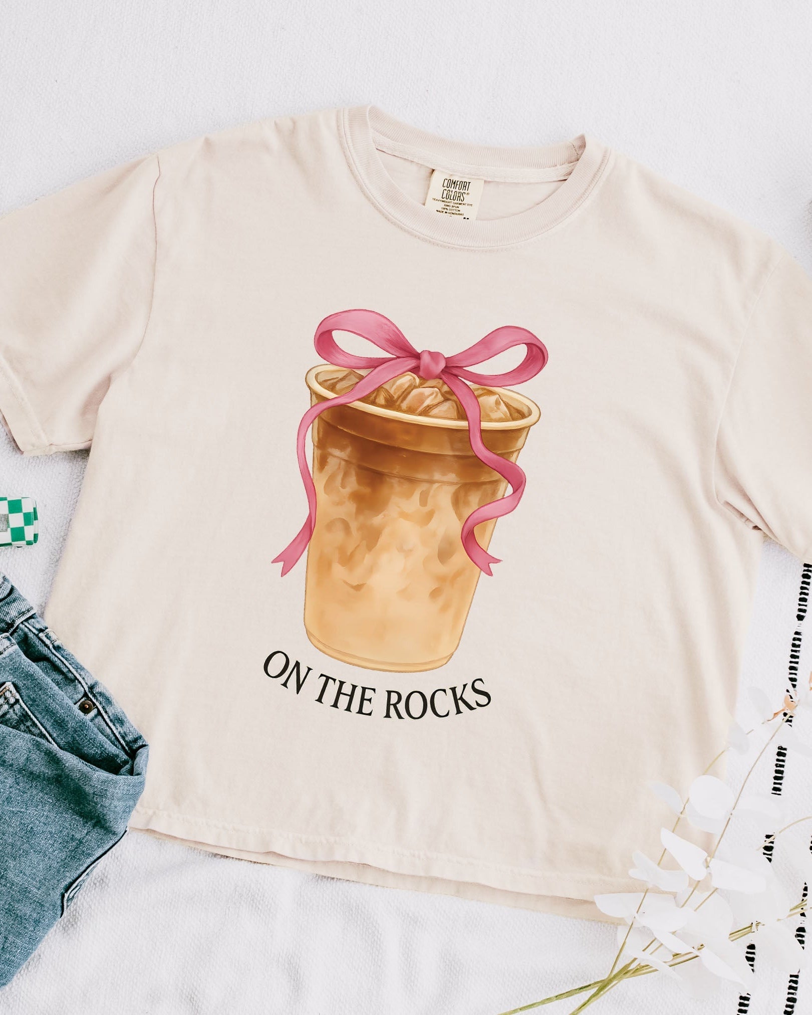 Women’s T-shirt, cream with pink bow latte graphic and 'ON THE ROCKS' text.