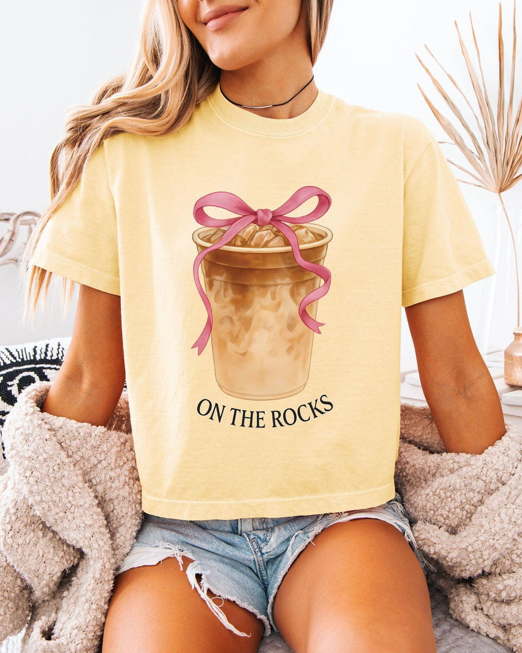 Women’s cropped T-shirt, light ivory with pink bow latte graphic and 'ON THE ROCKS'.
