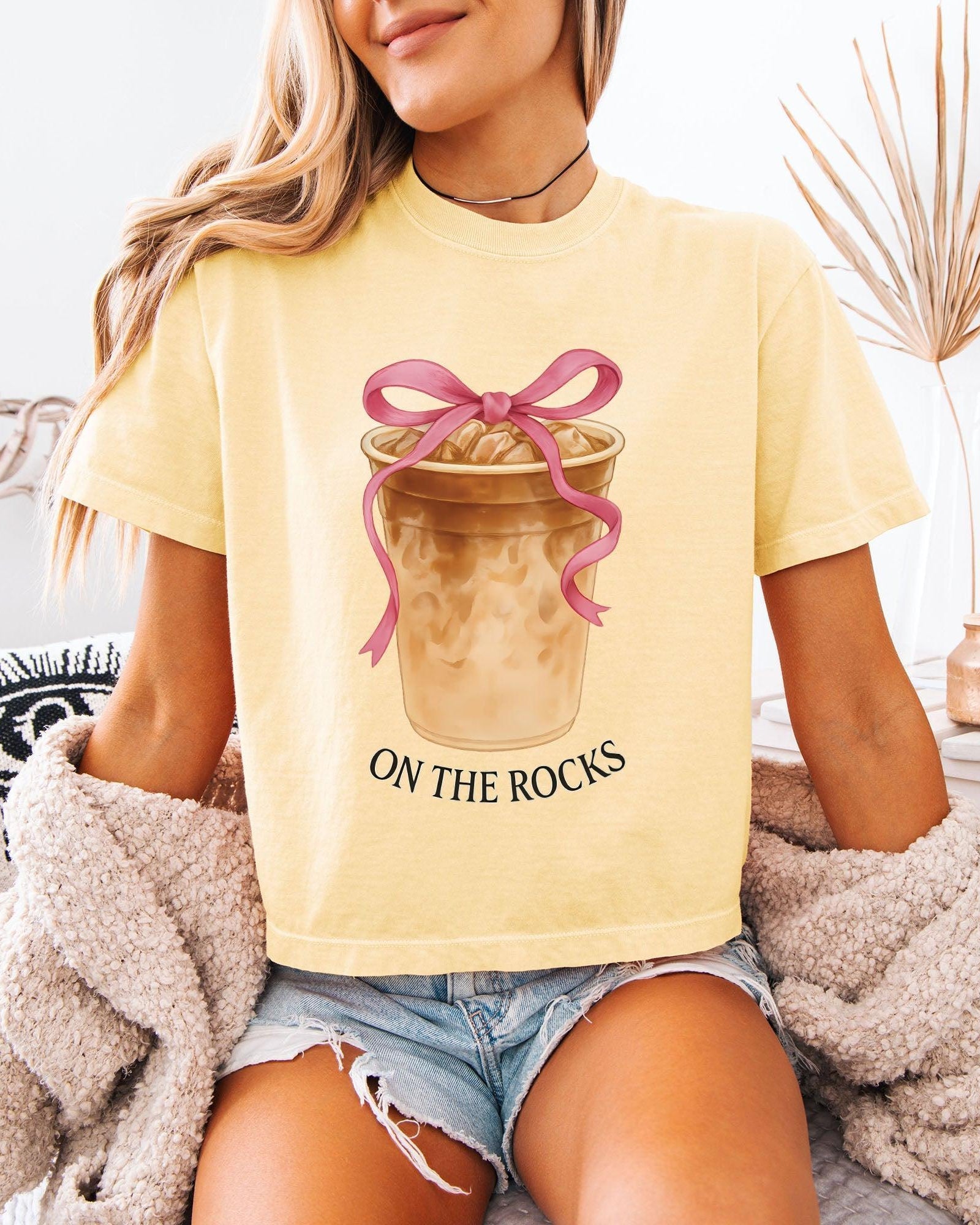 Women’s cropped T-shirt, light ivory with pink bow latte graphic and 'ON THE ROCKS'.