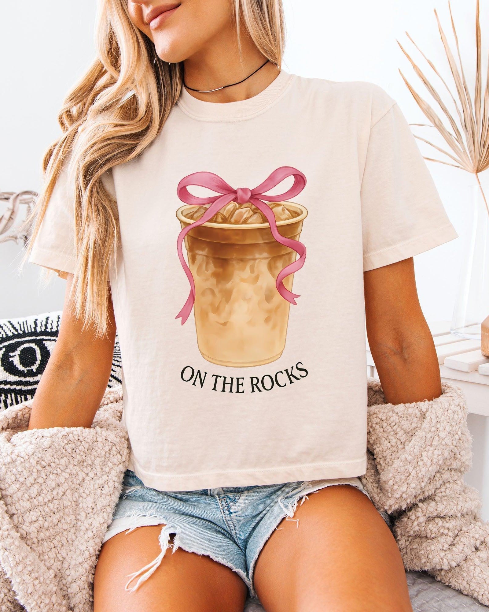 Women’s cropped T-shirt, pale white with pink bow latte graphic and 'ON THE ROCKS'.