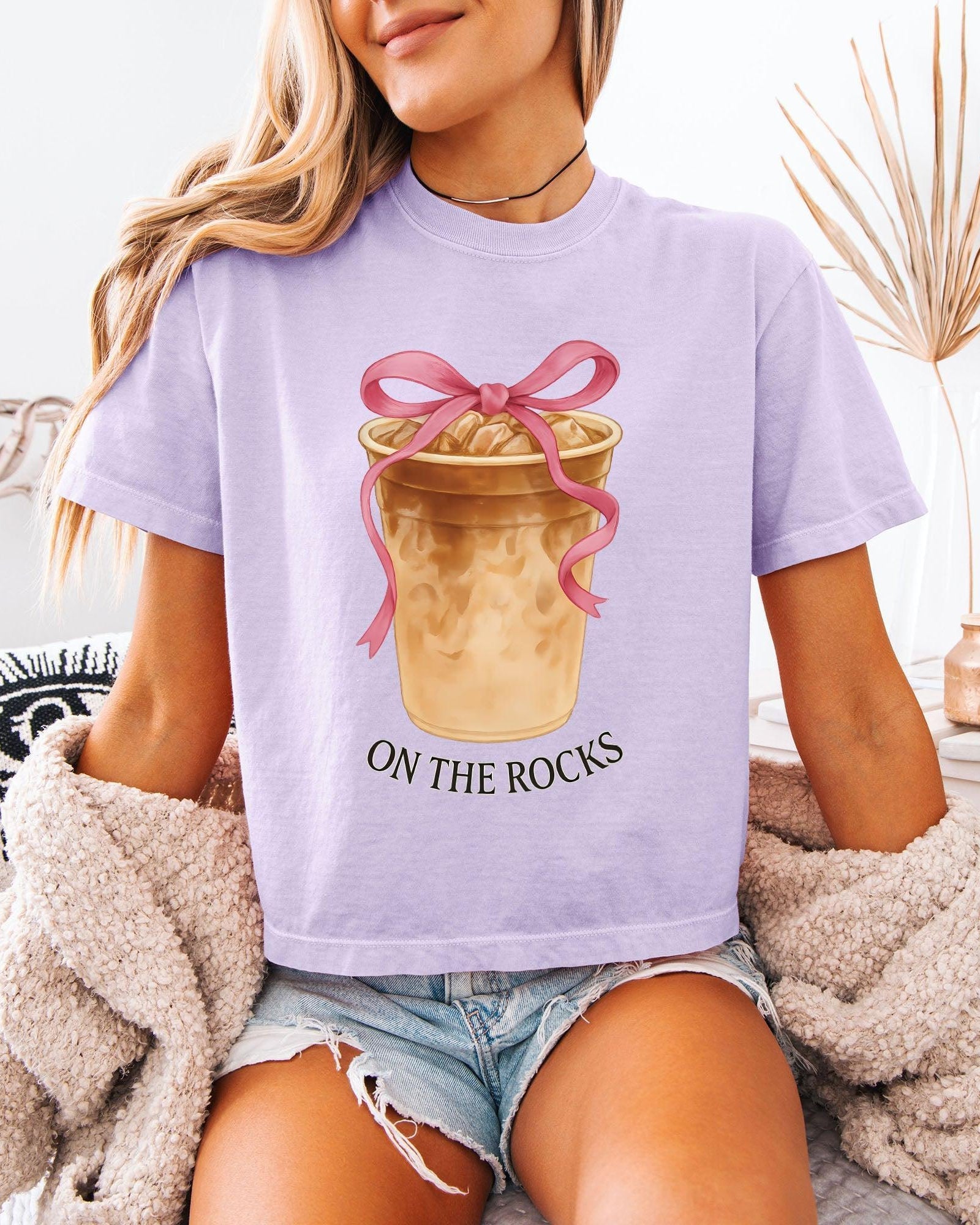 Women’s cropped T-shirt, lavender purple with pink bow latte graphic and 'ON THE ROCKS'.