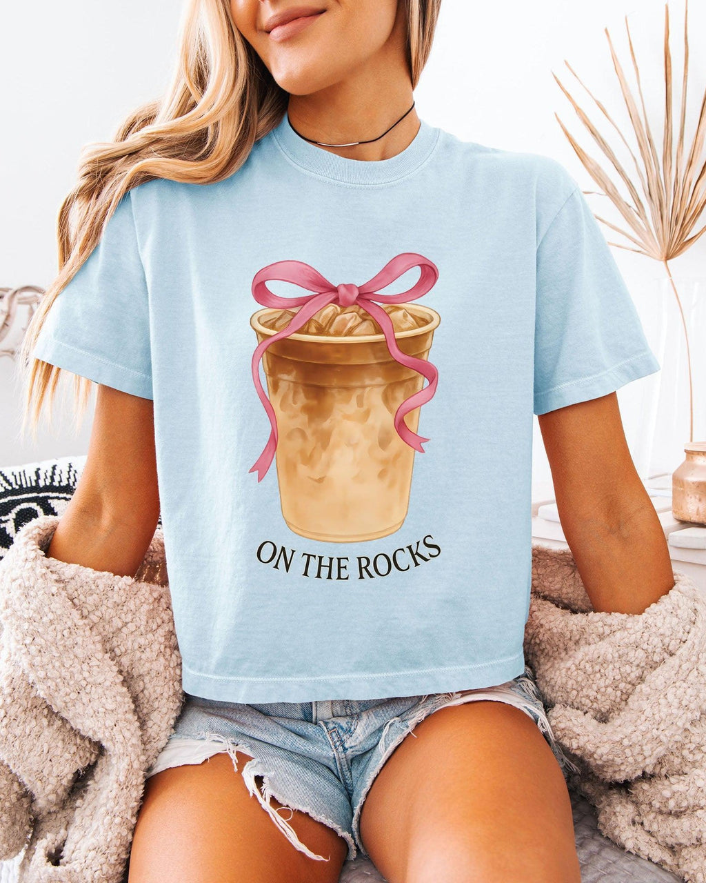 Women’s cropped T-shirt, light blue with pink bow latte graphic and 'ON THE ROCKS'.