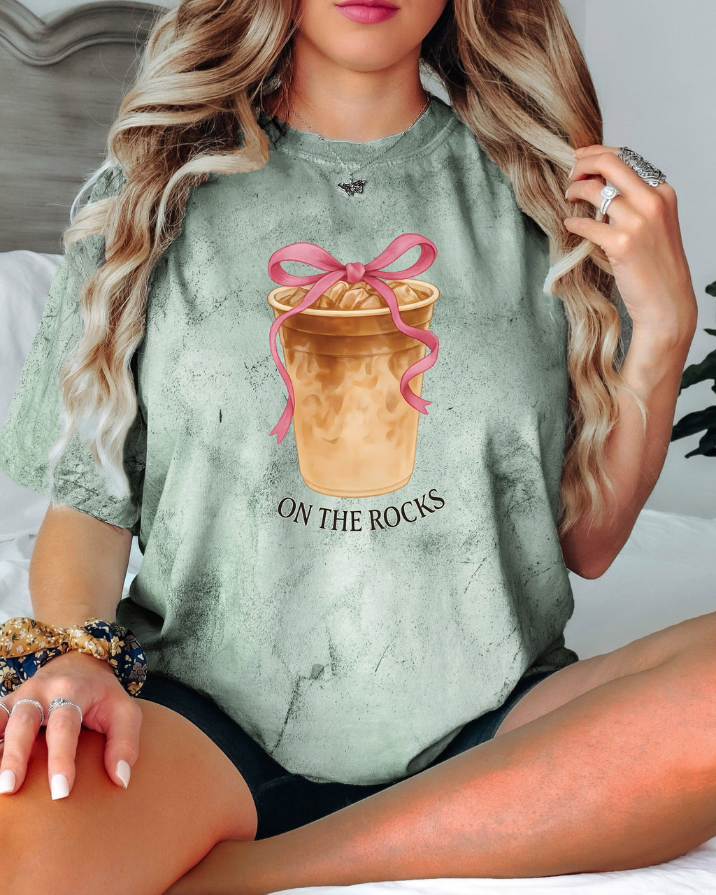 Garment-dyed green T-shirt with iced latte graphic, pink ribbon, and "On the Rocks" text