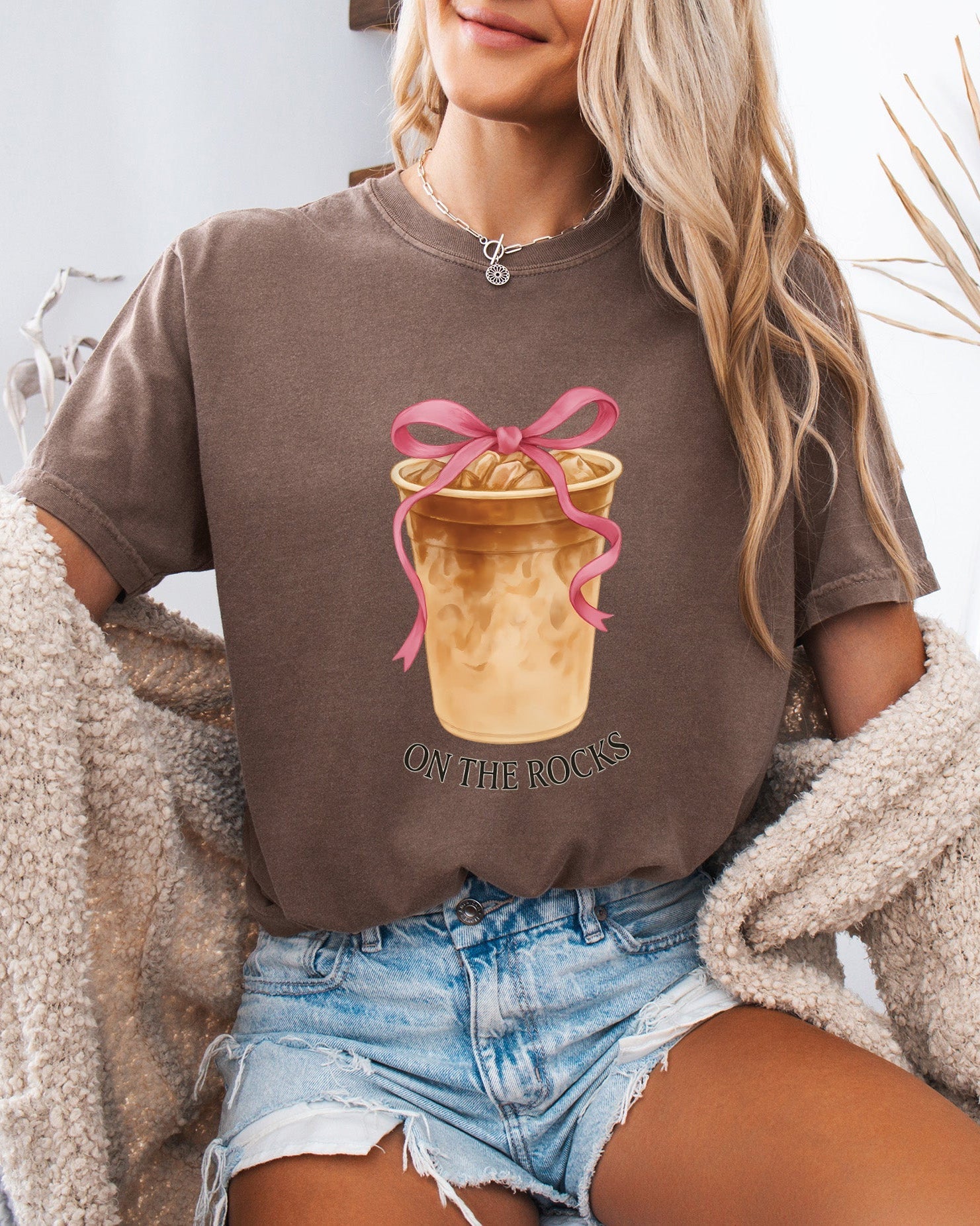 Brown T-shirt with iced latte cup graphic, pink ribbon bow, and "On the Rocks" text
