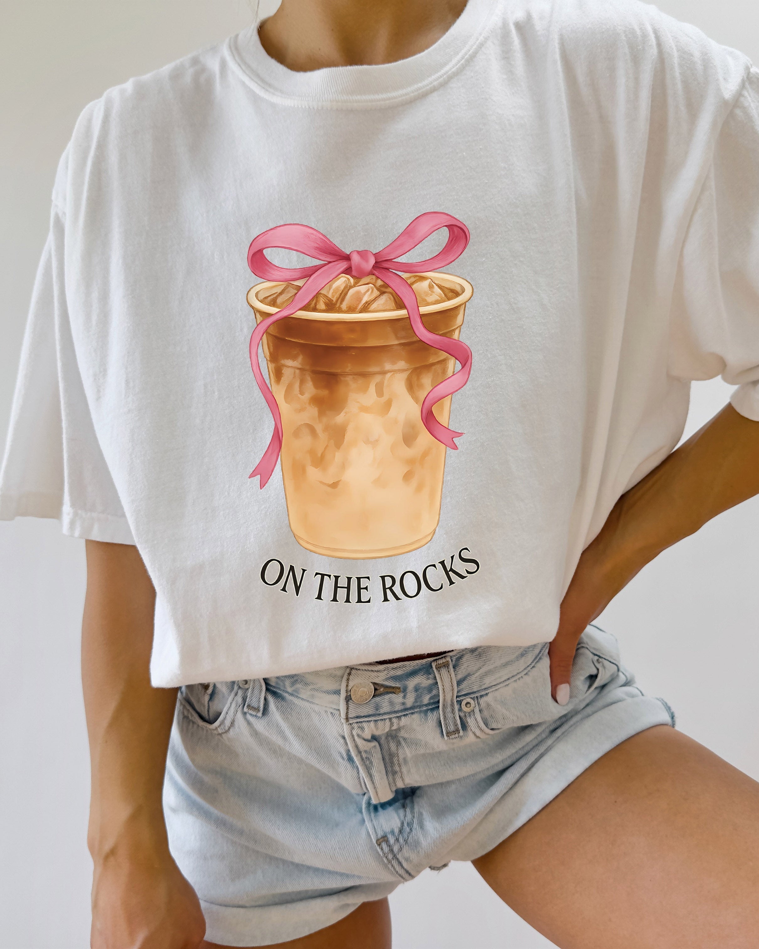 White iced latte graphic T-shirt with ribboned cup and “ON THE ROCKS” text
