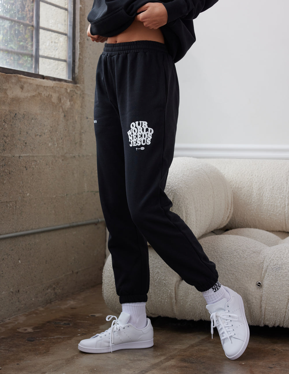 Black unisex sweatpants with Our World Needs Jesus logo on thigh and tapered cuff